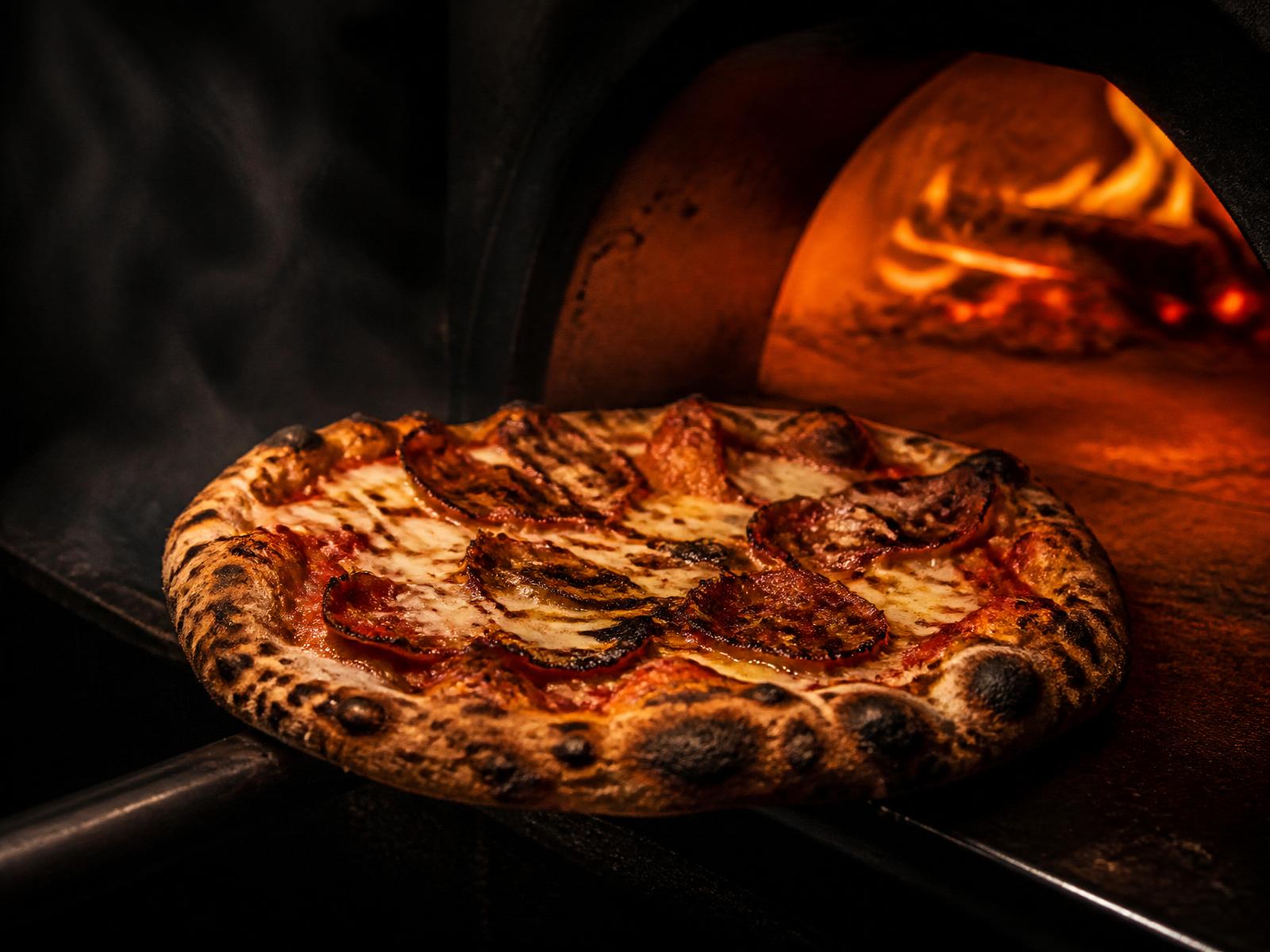Coal-fired pizza pulled from a glowing wood-fired oven